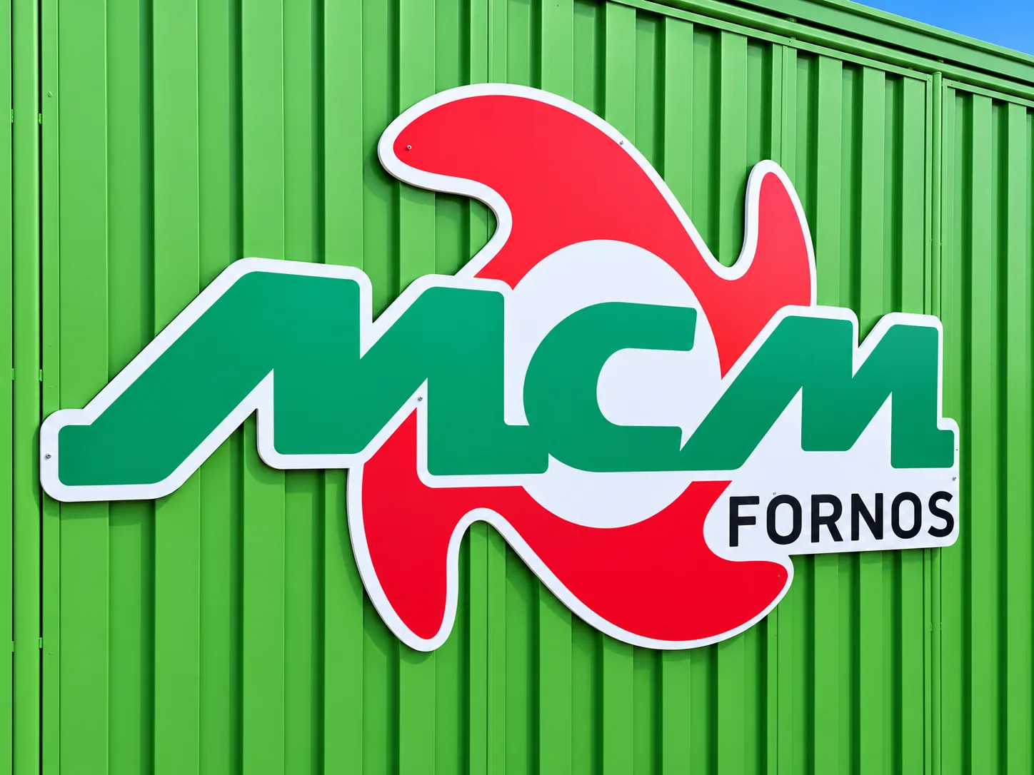 Letreiro recortado da MCM Fornos sobre parede metálica verde